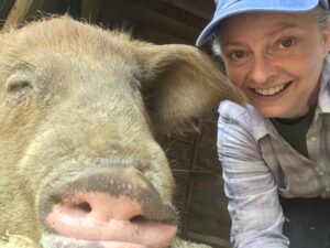Jennifer Brunk (a white woman) smiles alongside a pig who looks relaxed and content.